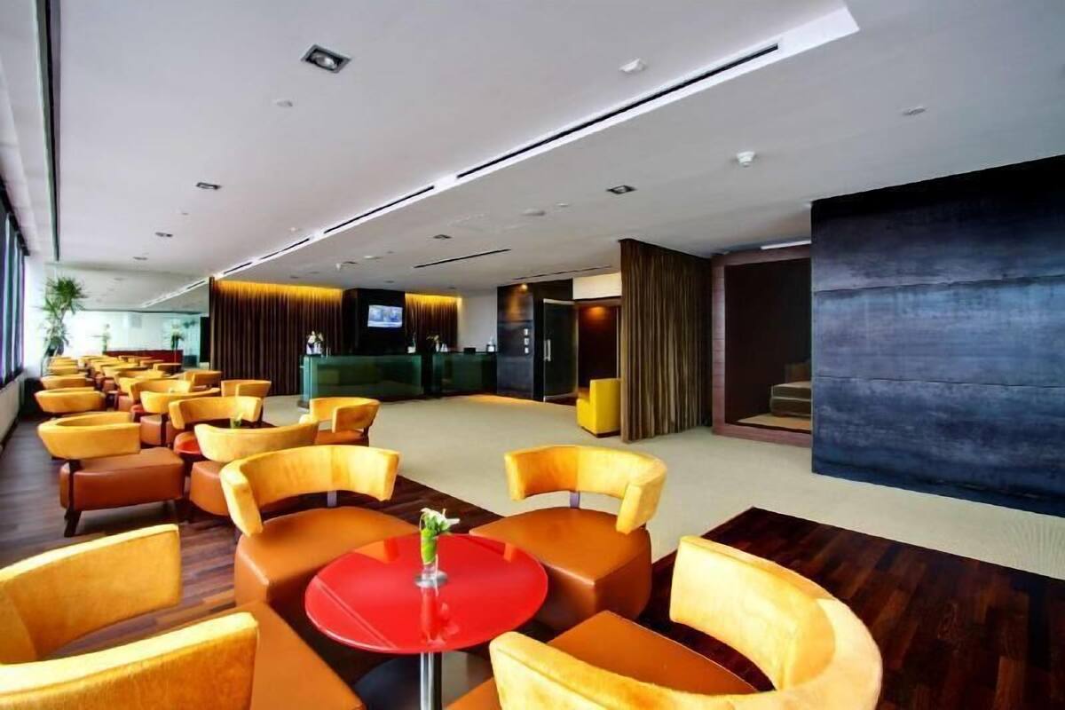 Un vestíbul d'hotel modern amb files de cadires grogues, un taulell vermell i una zona de recepció amb televisió.