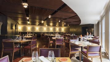 Um restaurante espaçoso com várias mesas e cadeiras, bem iluminado com iluminação pendente e um design de teto moderno.