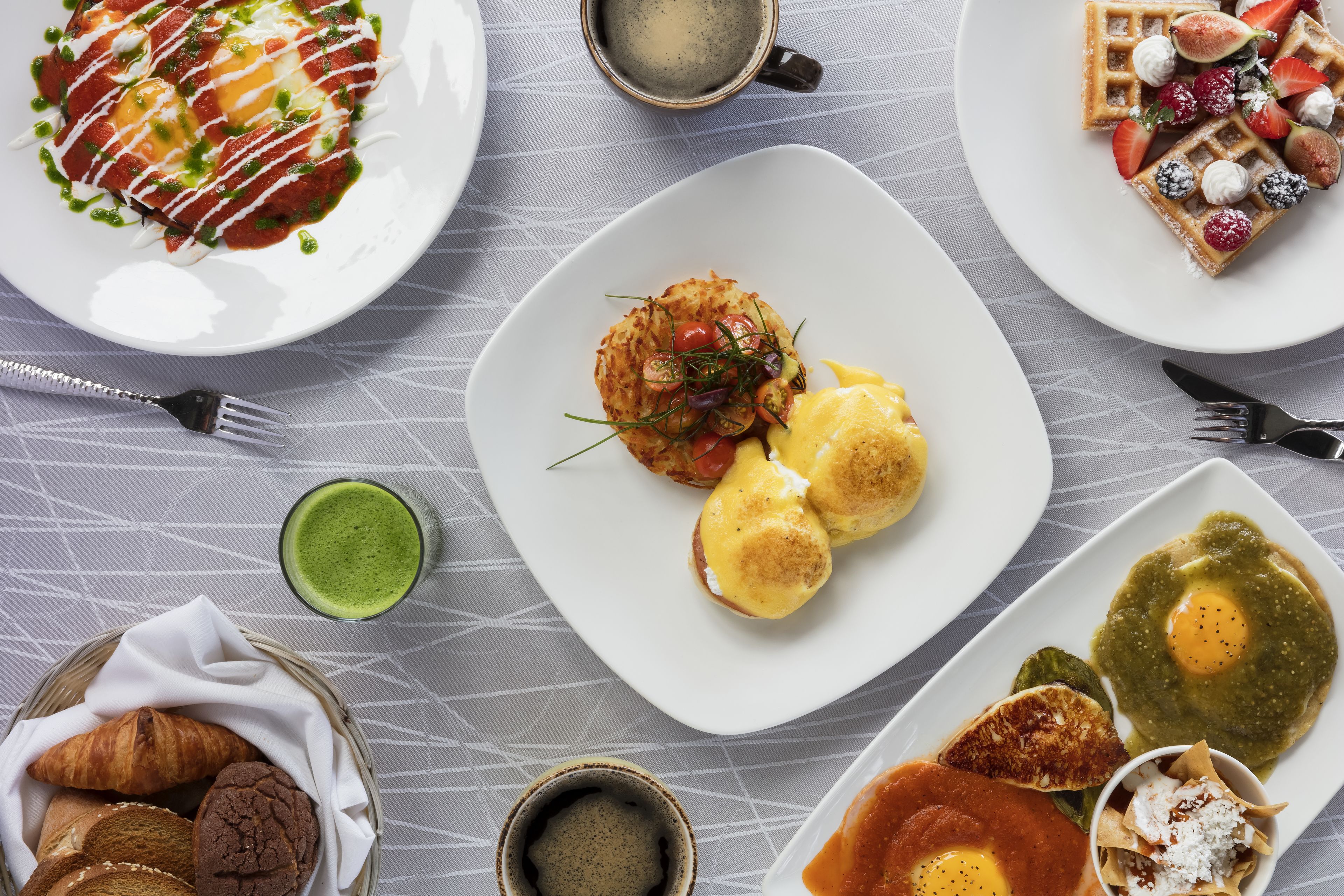 A breakfast buffet with various dishes including eggs, pastries, and a green beverage.