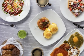 En morgenmadsbuffet med forskellige retter, herunder æg, bagværk og en grøn drik.