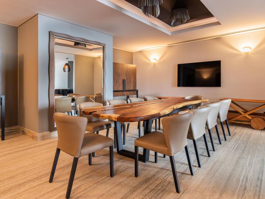A modern conference room with a long wooden table, multiple chairs, a large mirror, and a flat-screen TV mounted on the wall.
