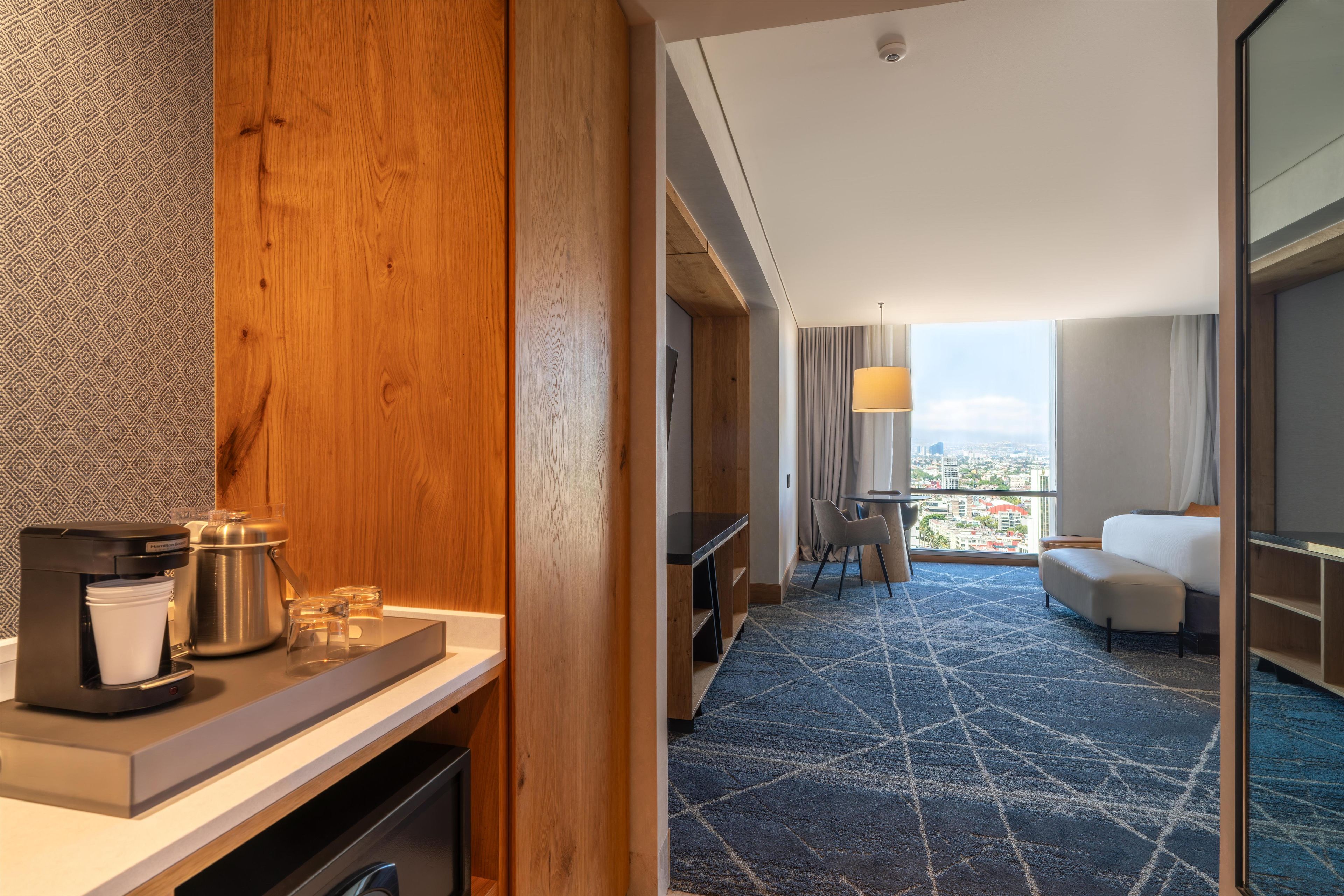 Habitación de hotel con una pared decorativa de madera, una cafetera, un área de comedor con vistas y un sofá.