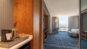 Habitación de hotel con una pared decorativa de madera, una cafetera, un área de comedor con vistas y un sofá.
