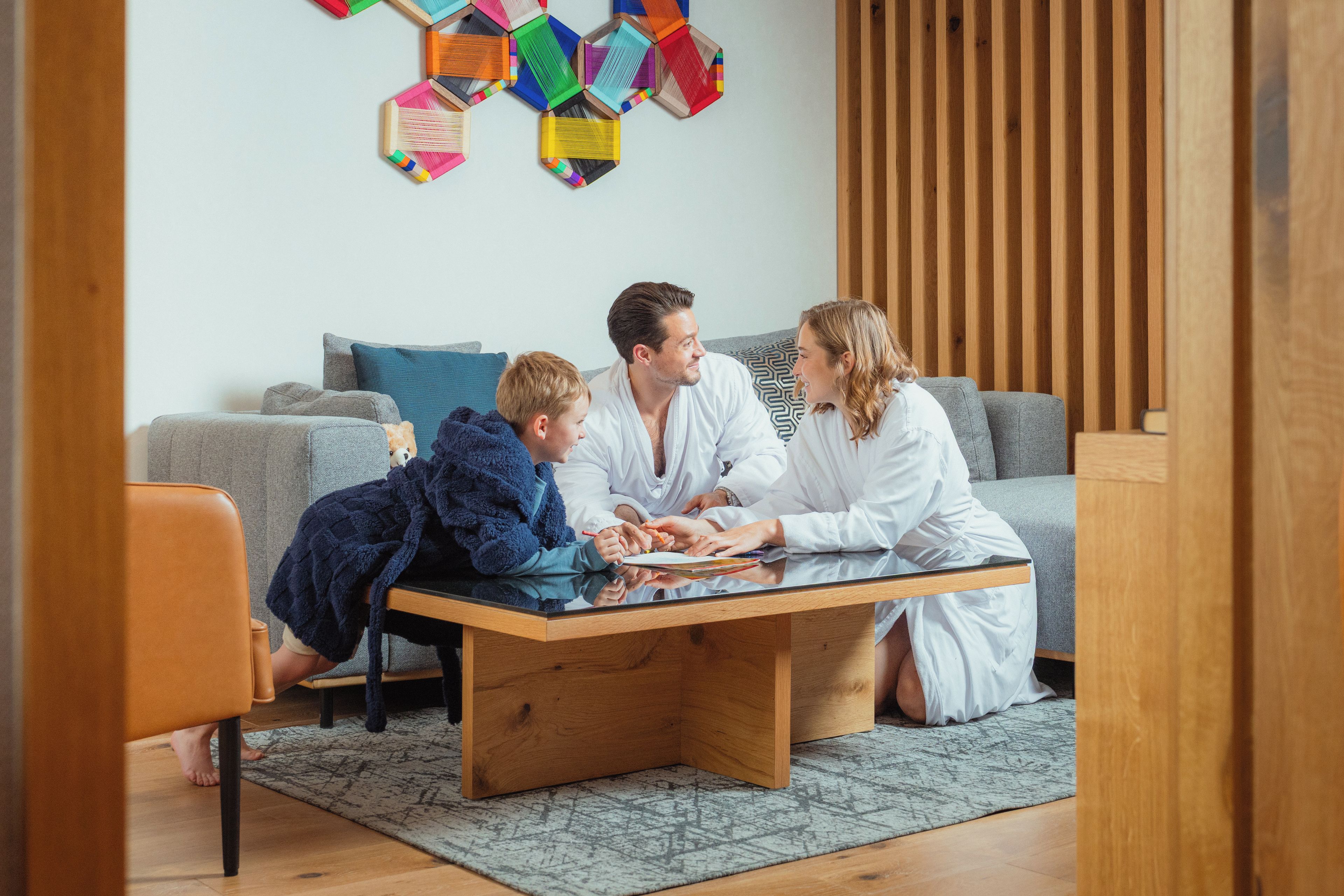 Una famiglia di quattro persone seduta a un tavolo di legno in un soggiorno moderno, con un divano grigio e un tappeto decorato.