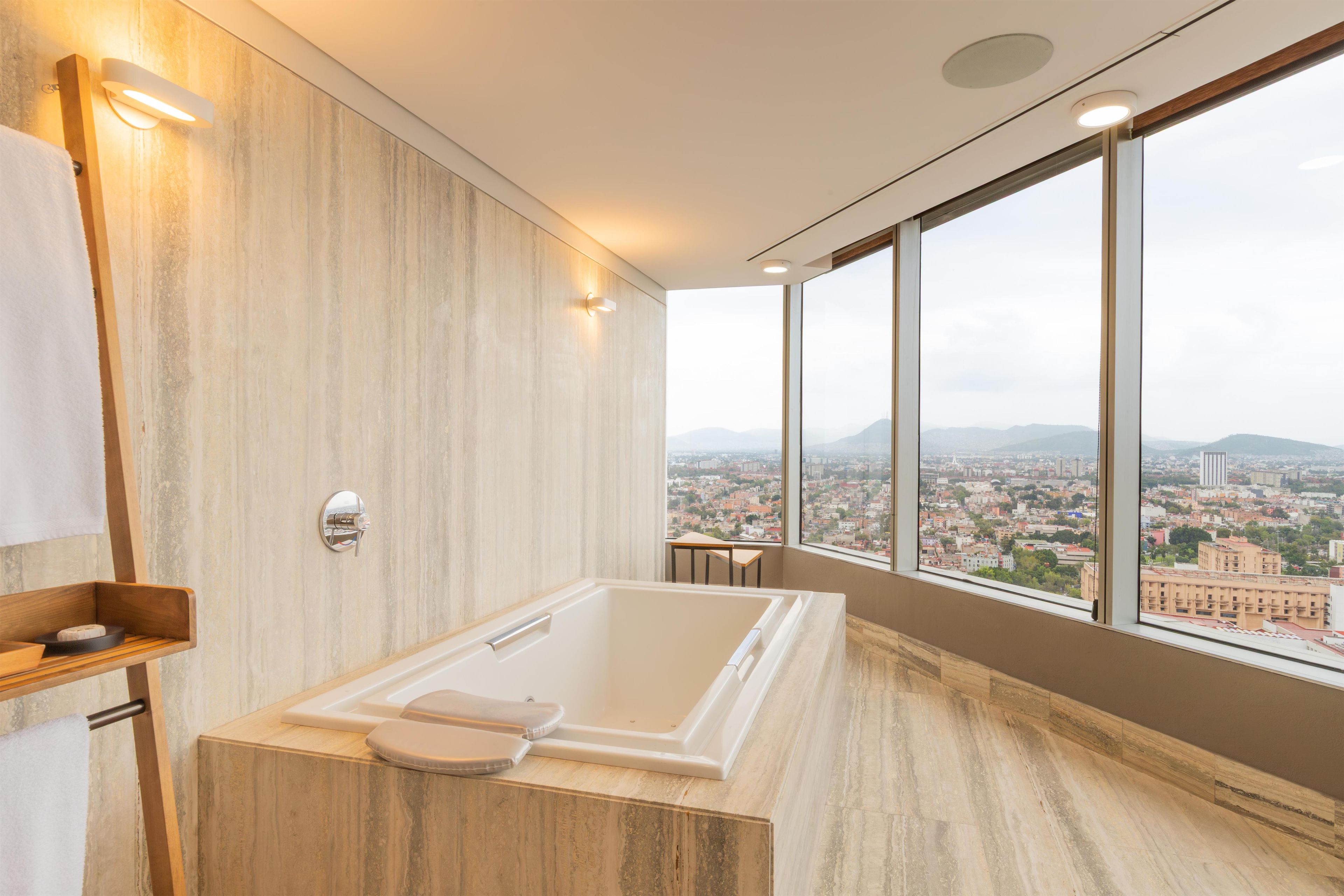 Un baño moderno con una bañera grande, paneles de madera en la pared y vistas a la ciudad a través de amplias ventanas.