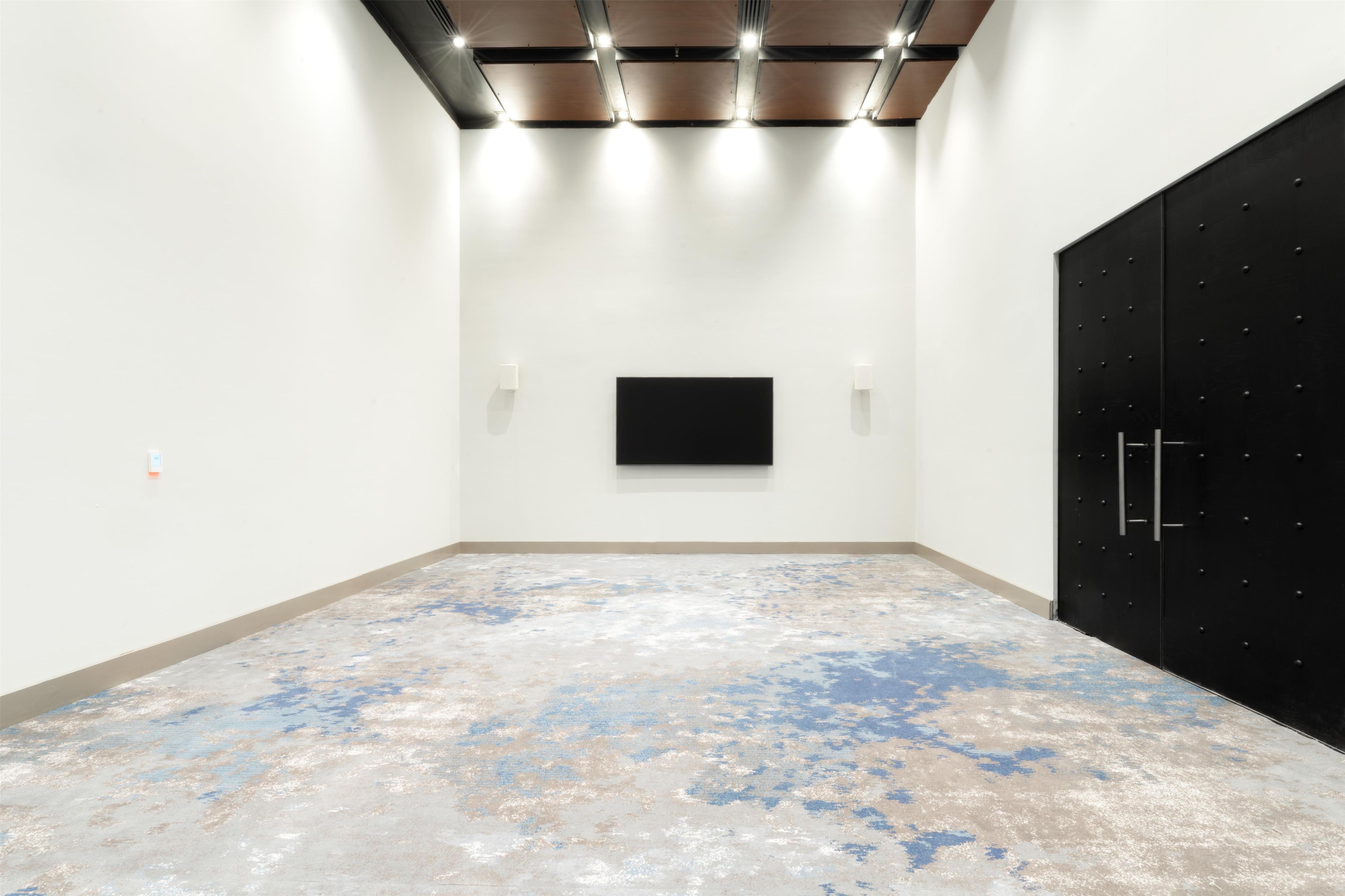 A room with a flat-screen TV mounted on the wall, a black wardrobe, and a textured floor.
