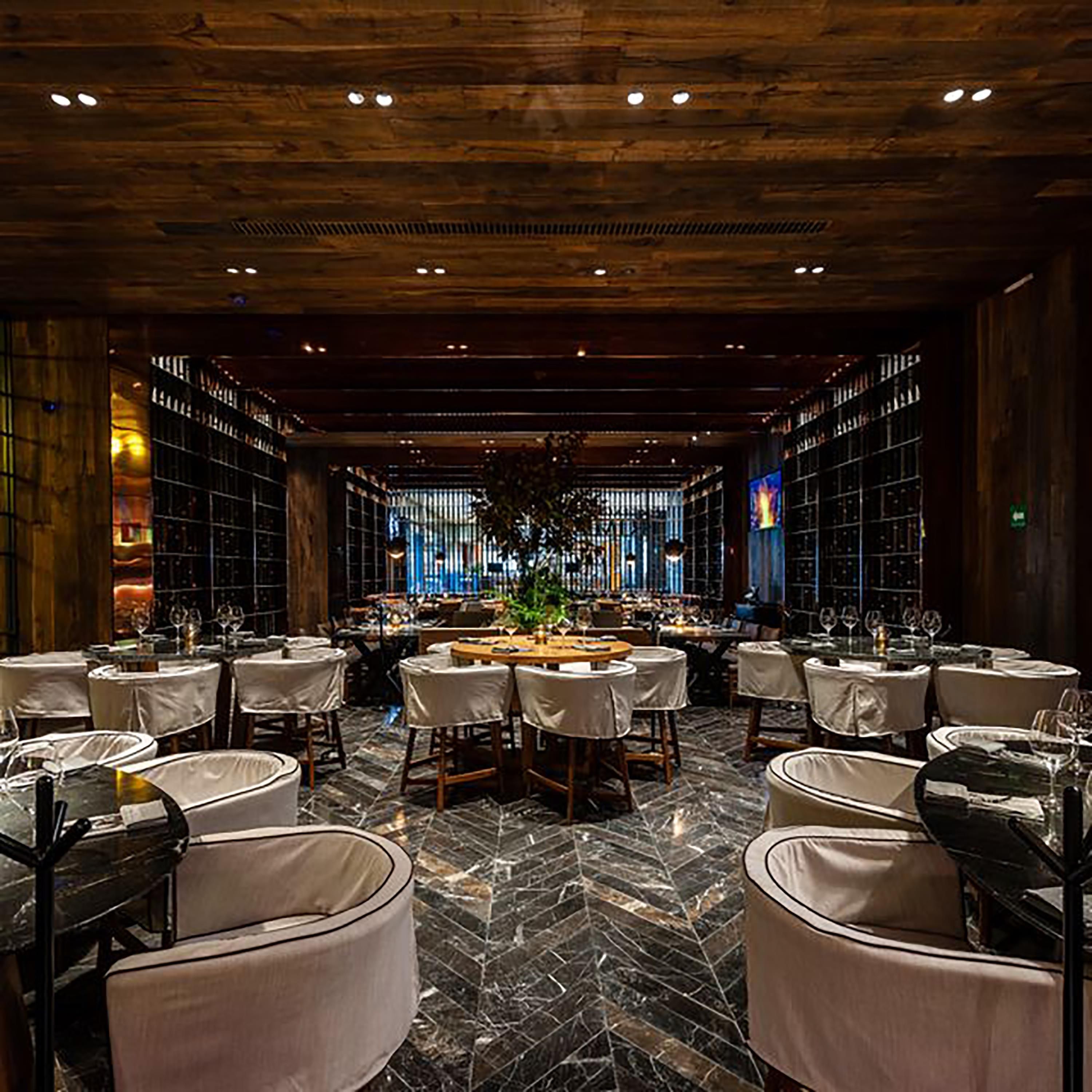 A restaurant with a central bar, multiple tables, and a herringbone floor pattern.