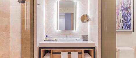 A modern bathroom with a glass-enclosed shower, a white sink with a mirror above, and a wooden shelf with towels.