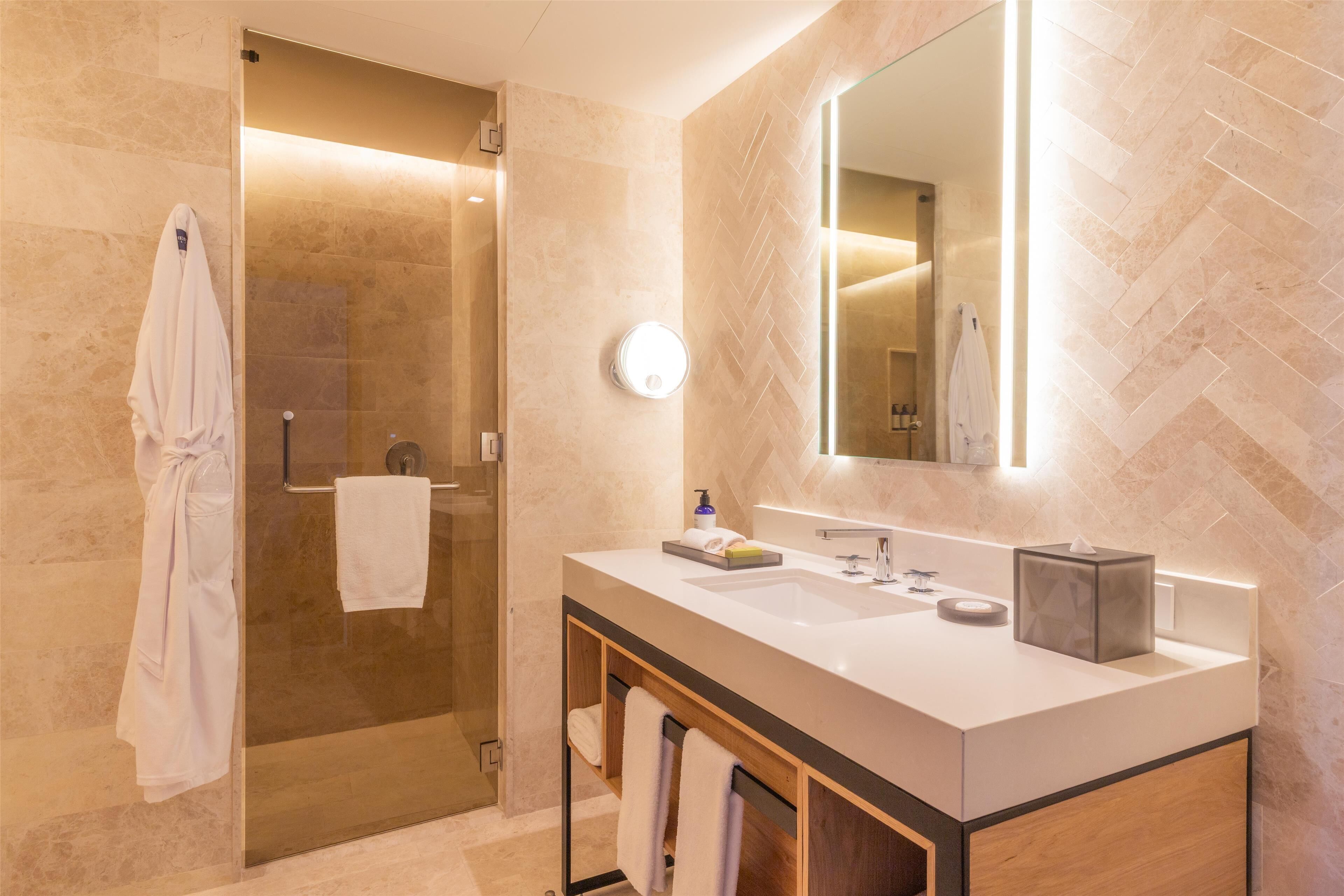 A modern bathroom with a glass shower enclosure, a large mirror, and a white vanity with a sink and towel rack.