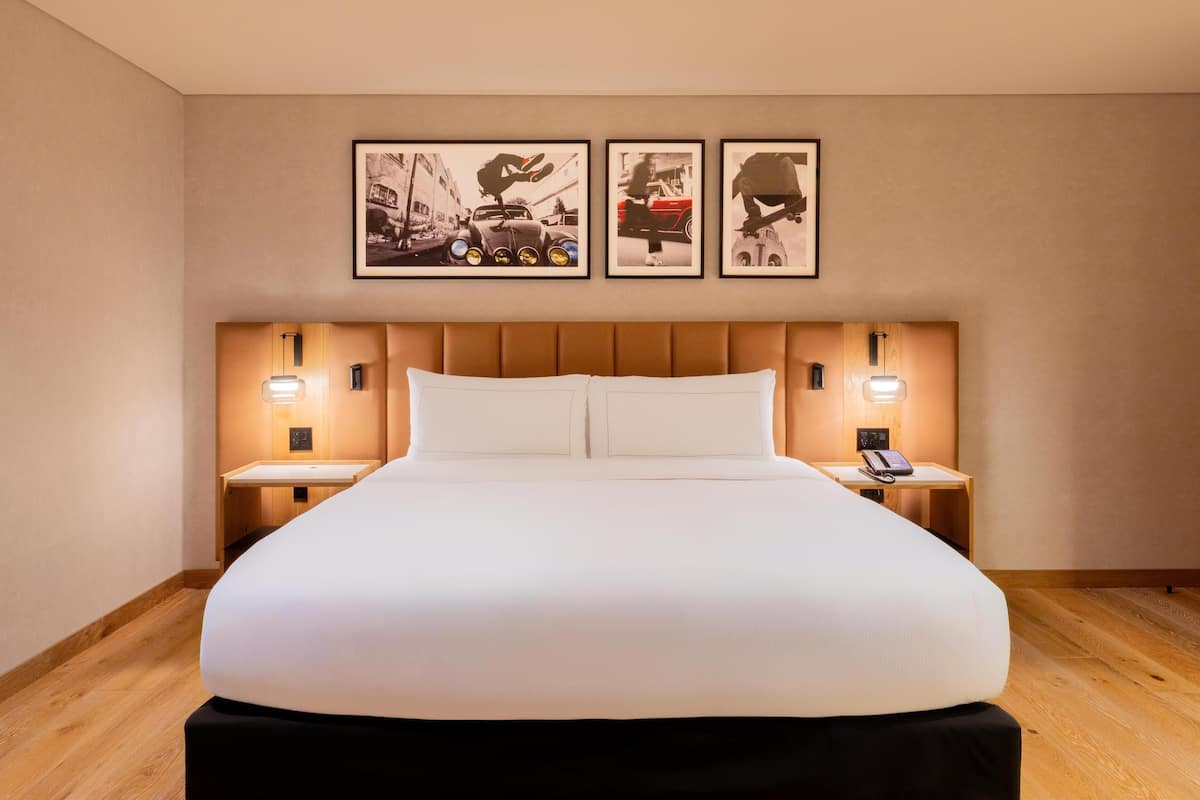 Una habitació d'hotel amb un llit gran, dues taules de nit amb làmpades i tres quadres a la paret.