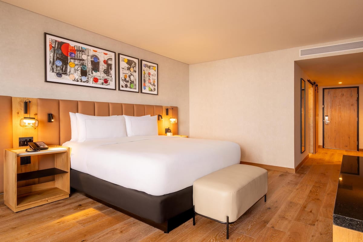 Una habitació d'hotel amb un llit gran, vetustats de fusta, una taula petita i un banc. Hi ha tres quadres emmarcats a la paret sobre el llit.