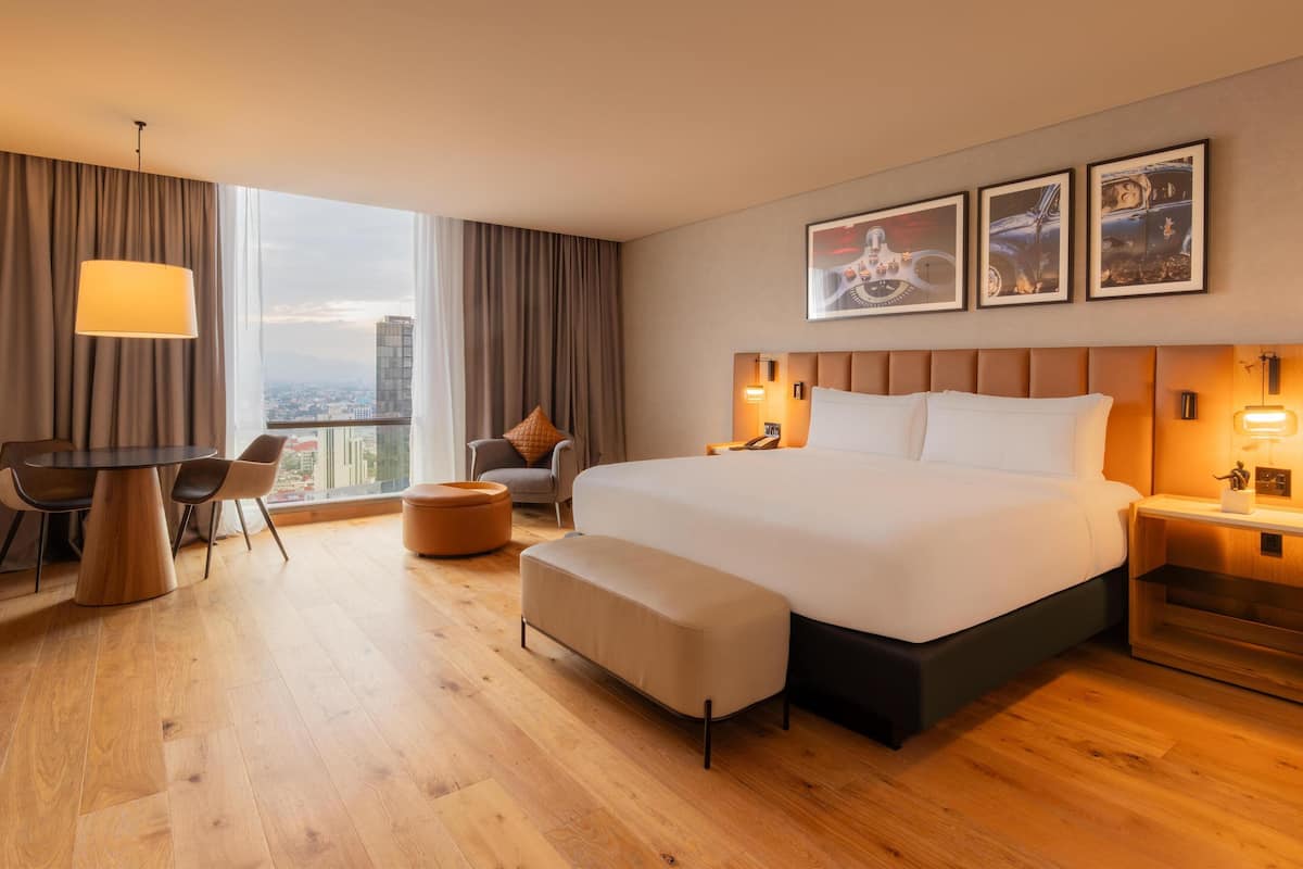 Una habitació d'hotel moderna amb un llit gran, una taula de dinar i vista a la ciutat.