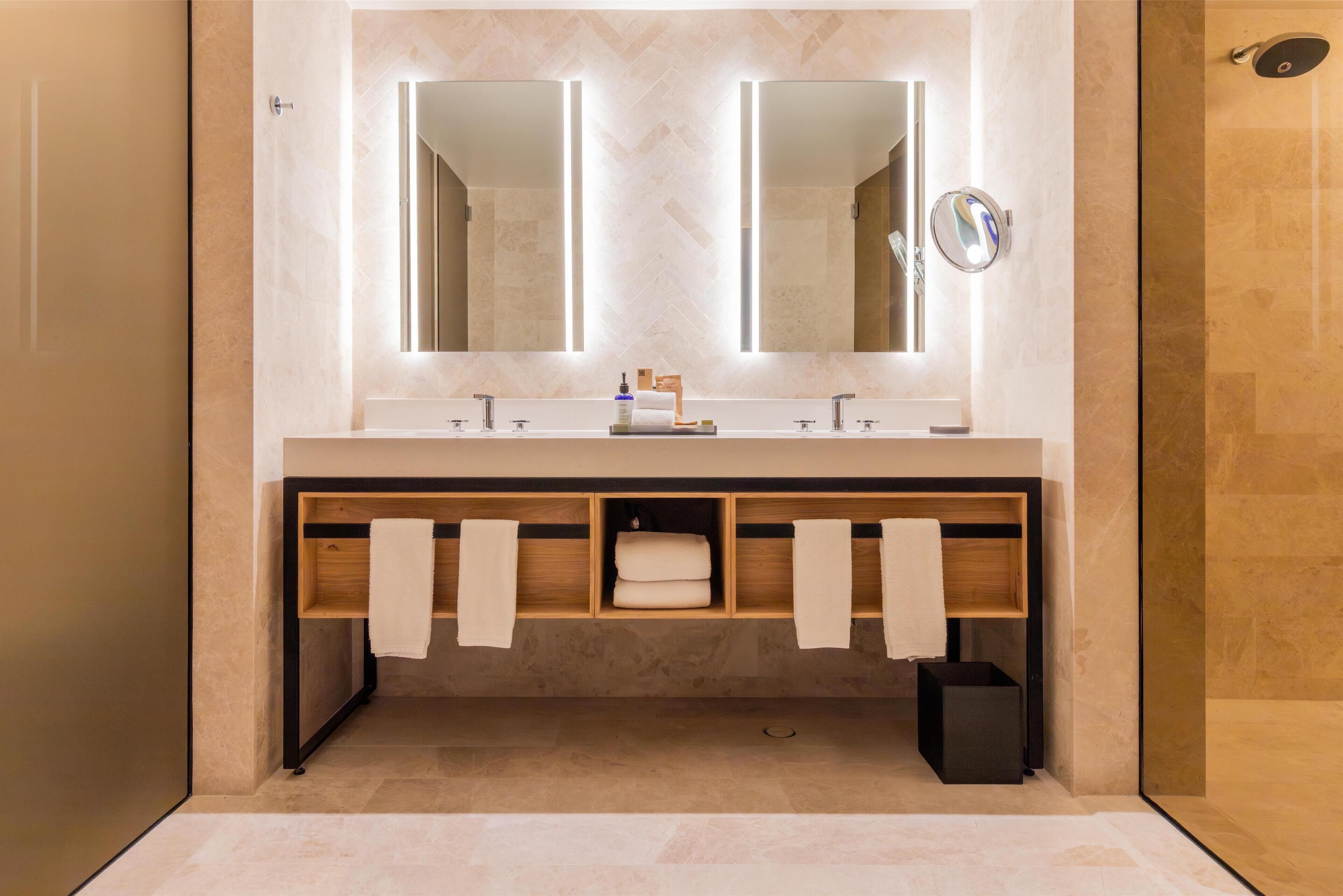 A modern bathroom with a double vanity, two mirrors, and a built-in shelf with towels.