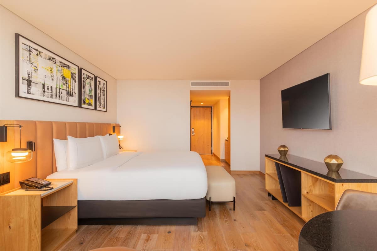 Una habitació d'hotel amb un llit gran, taules de nit, un escriptori, un televisió de pantalla plana i obra d'art a la paret.