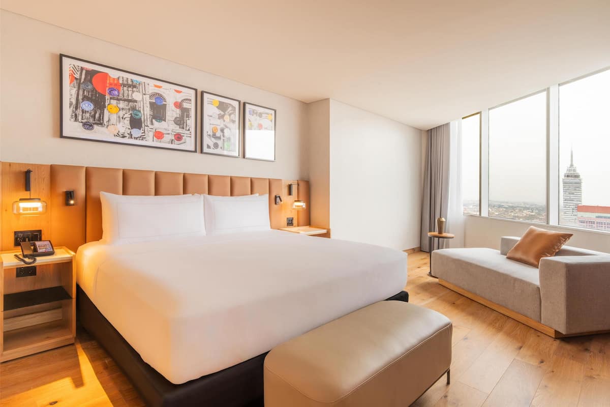 Habitació d'hotel moderna amb un llit gran, un sofà i vista a la ciutat.