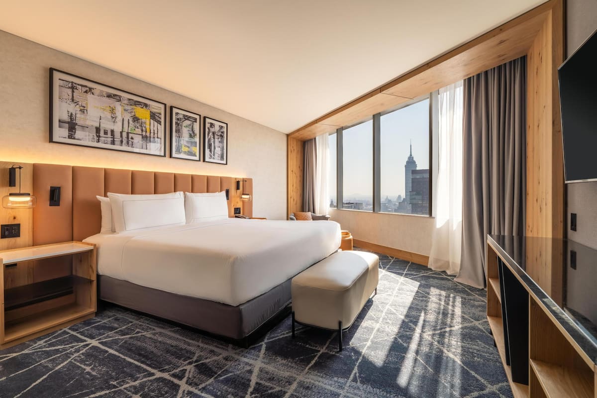 Habitació d'hotel amb un llit gran, televisió, escriptori i finestra que dona a la vista de la ciutat.