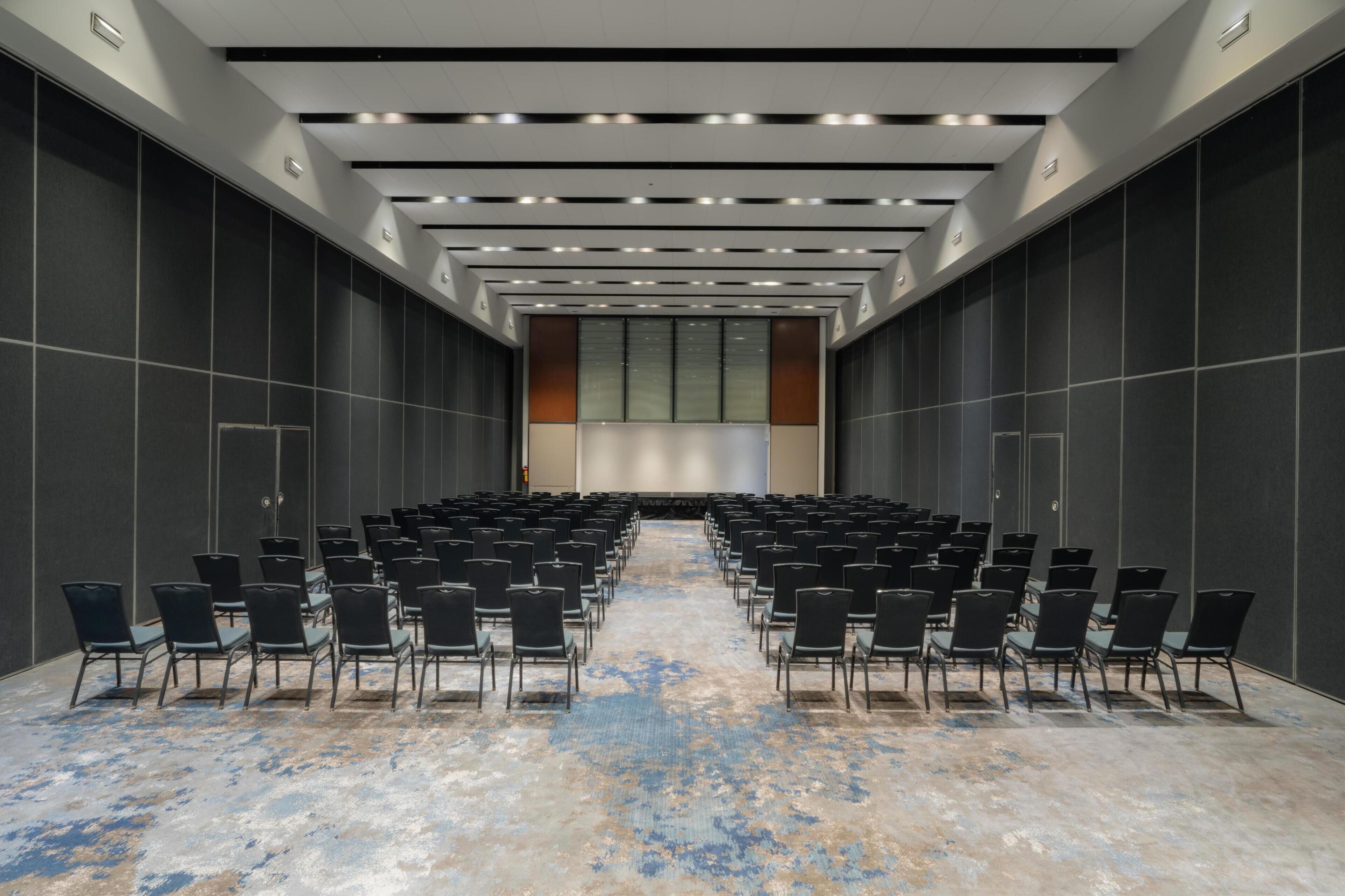 A conference room with rows of chairs, a stage, and a large screen.
