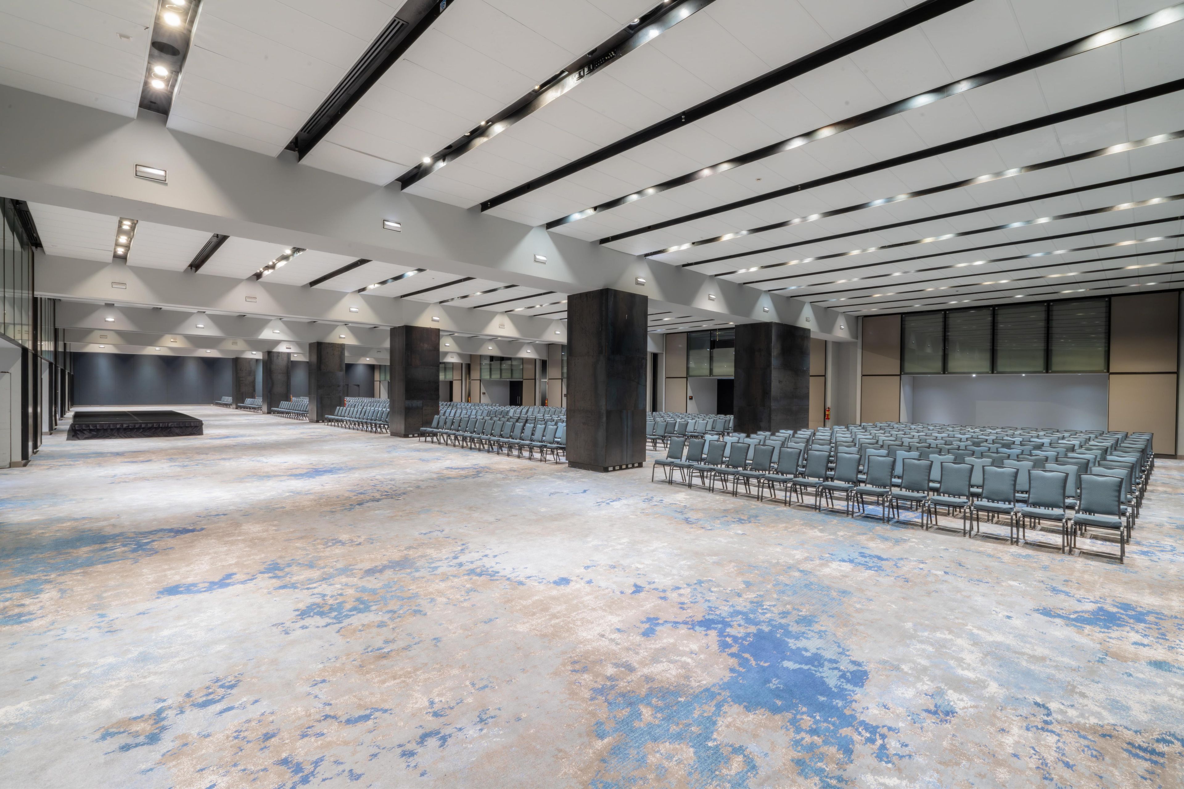 A spacious indoor area with rows of chairs, a high ceiling with linear lighting, and a concrete floor.