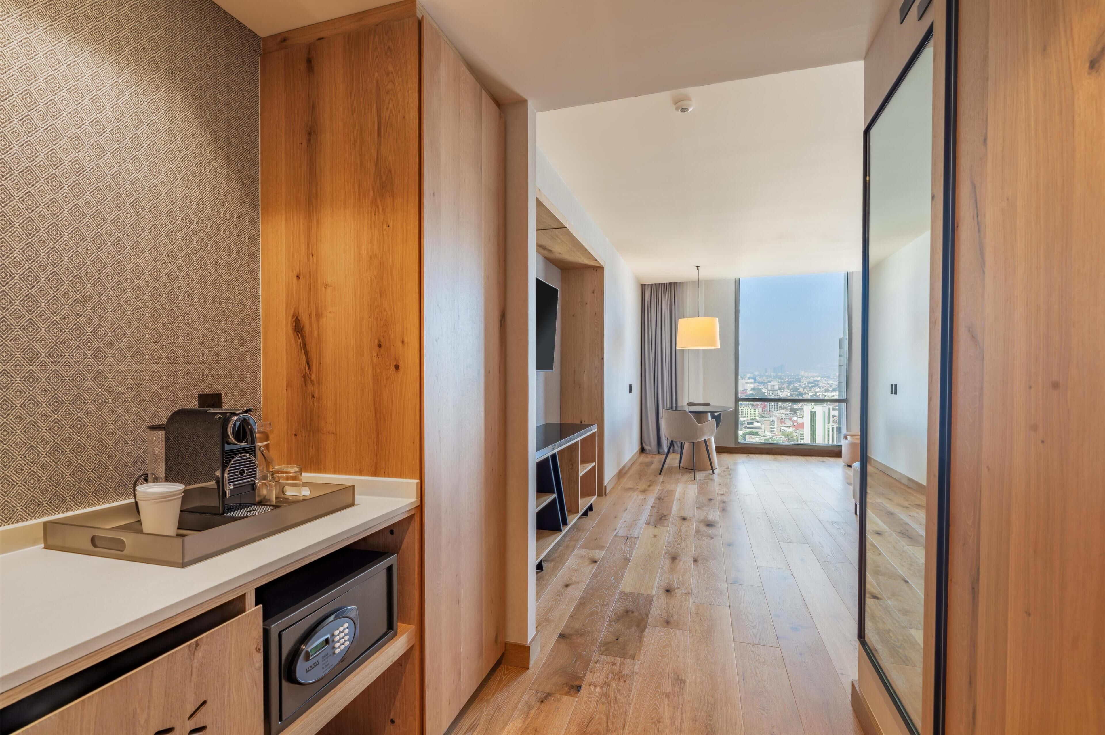 Quarto de hotel moderno com cozinha compacta, televisão, área de refeições e varanda com vista para a cidade.