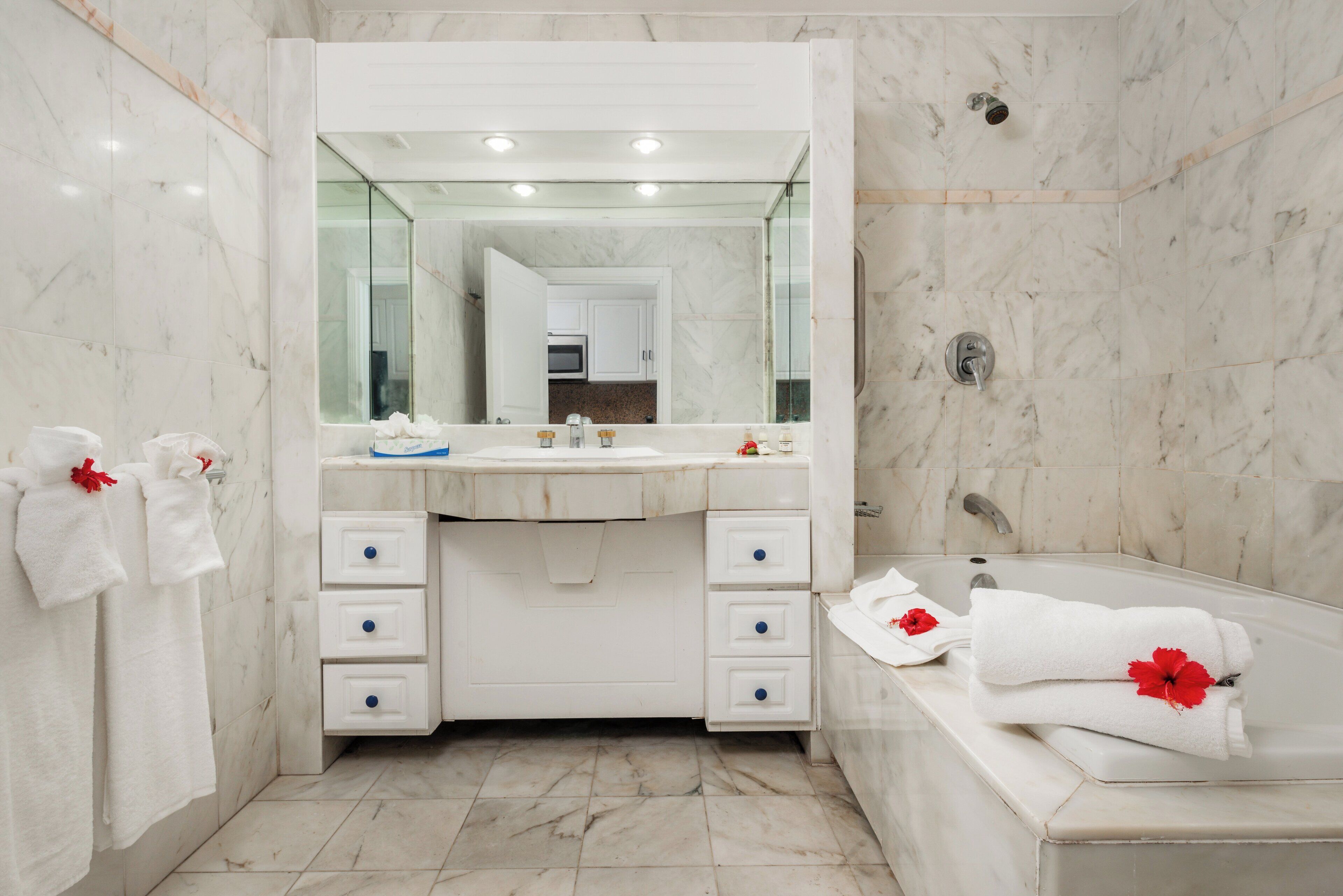 A modern bathroom with a marble vanity, a large mirror, a bathtub, and towels with red flowers.