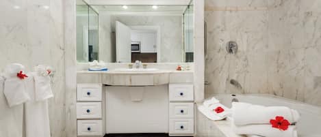 A modern bathroom with a marble vanity, a large mirror, a bathtub, and towels with red flowers.