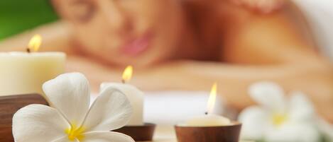 Un ambiente de spa con velas y flores sobre una bandeja de madera.
