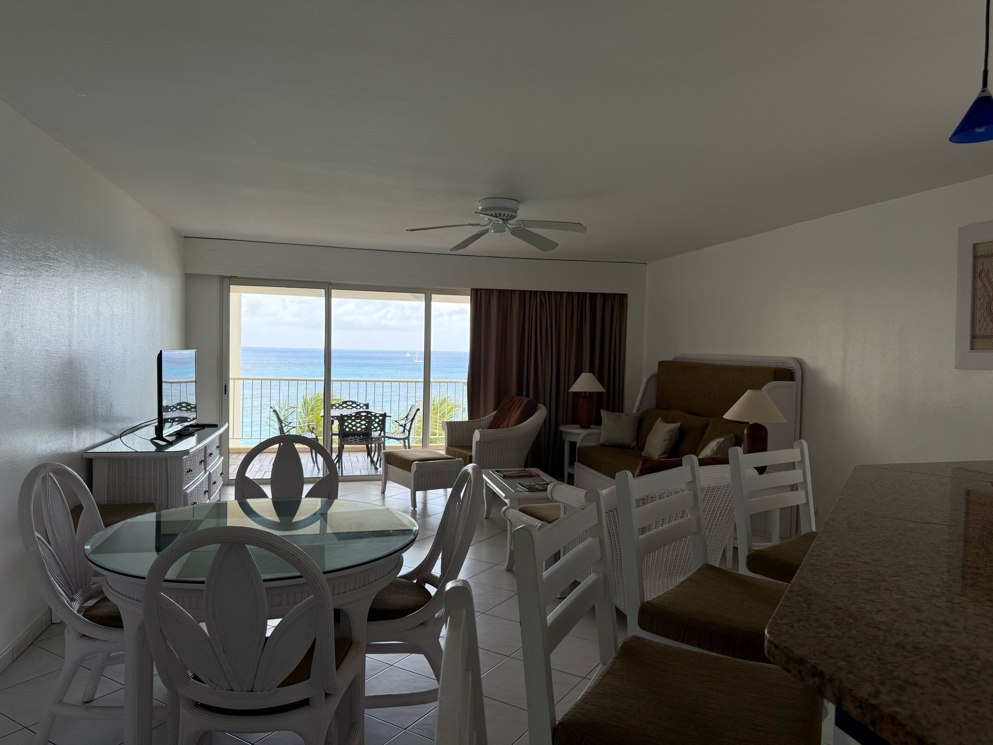 A hotel room with a balcony, a dining area, and a seating area with a view of the ocean.