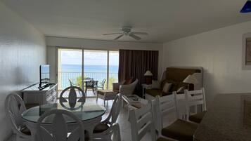 A hotel room with a balcony, a dining area, and a seating area with a view of the ocean.