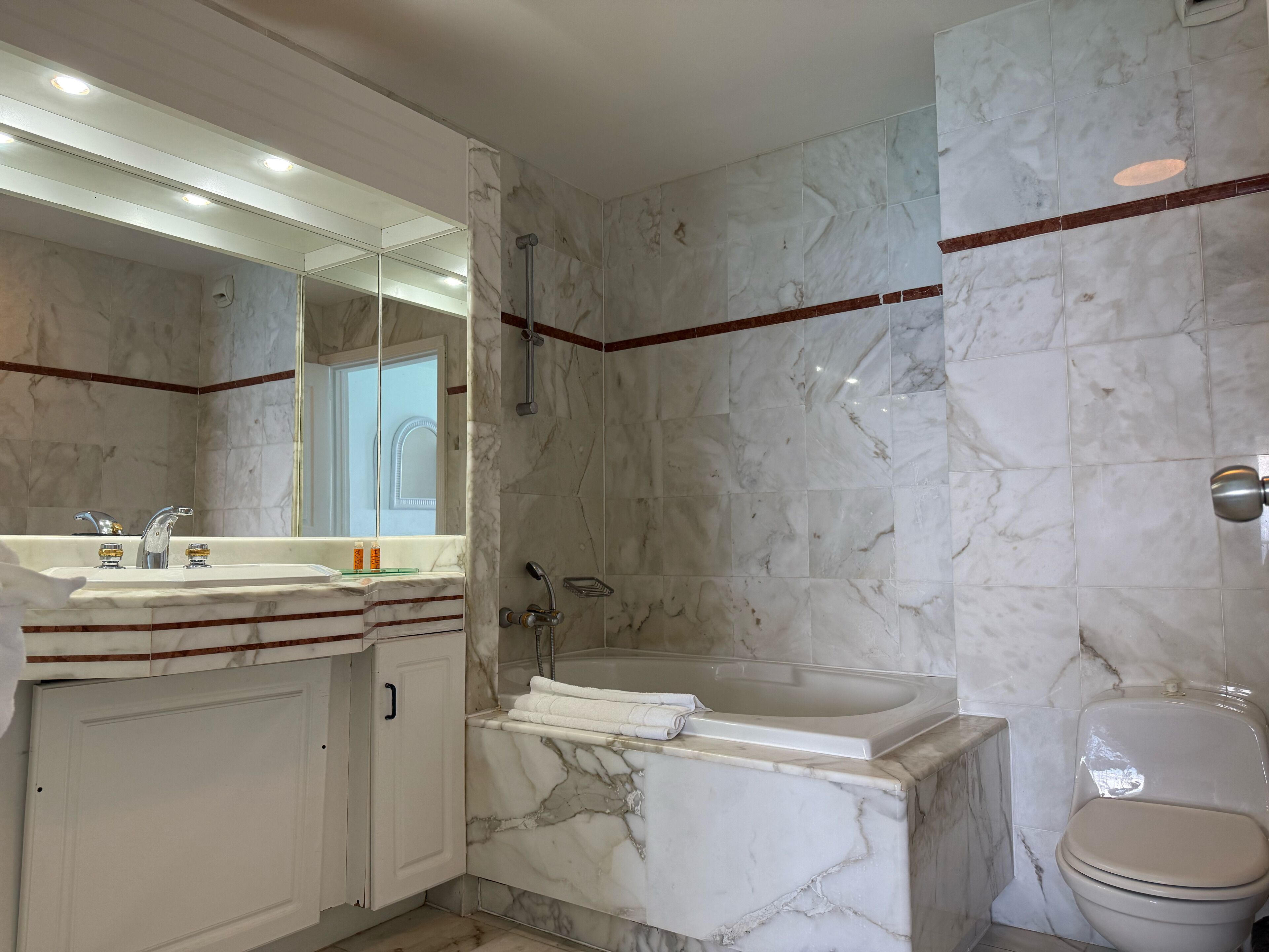 A modern bathroom with a marble sink, a bathtub, and a toilet.