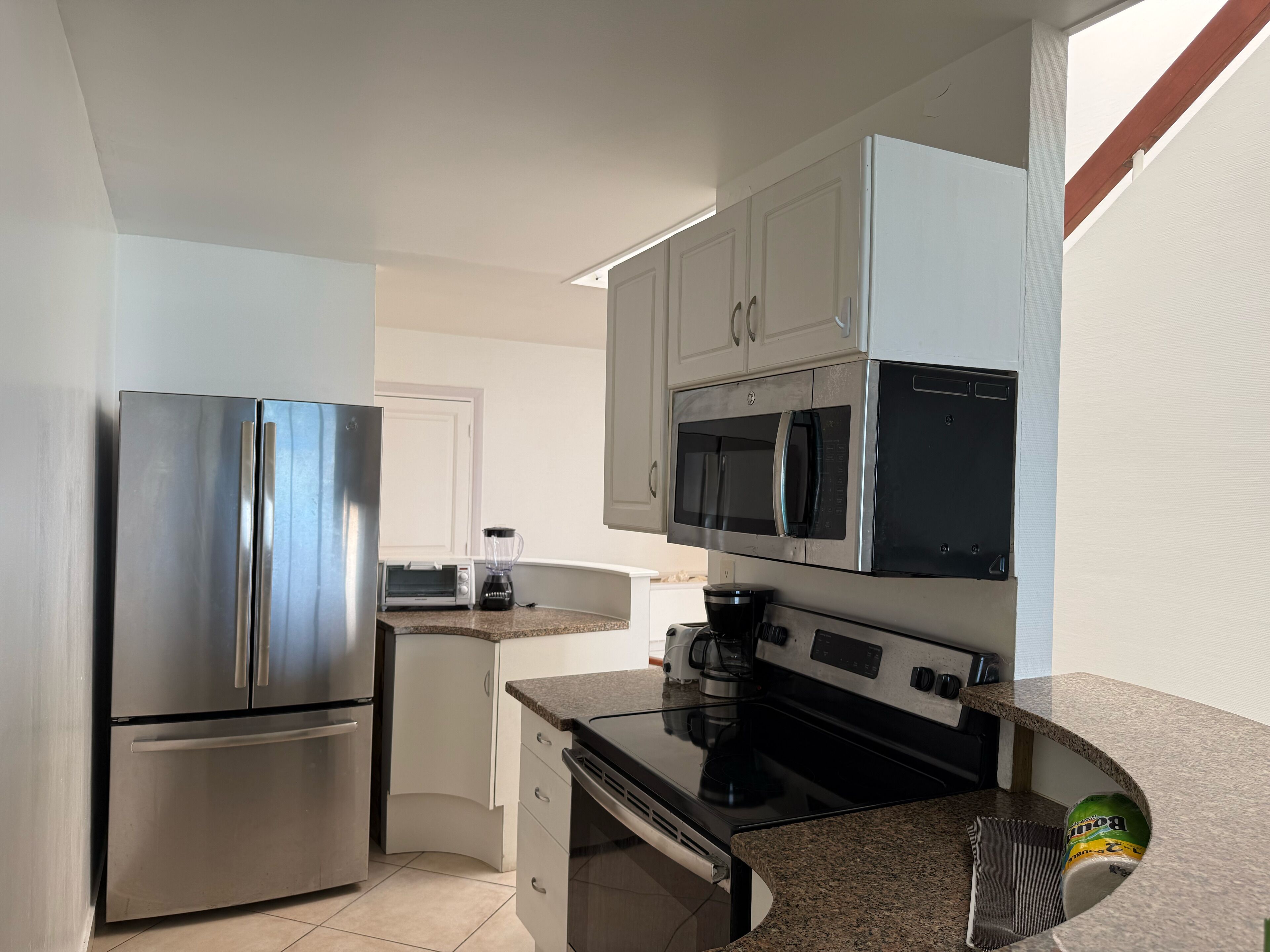 Eine kompakte Küche mit Edelstahlkühlschrank, Mikrowelle, Backofen und Toaster.