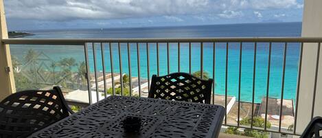 Un balcon avec une table et des chaises donnant sur un océan turquoise et un ciel dégagé.