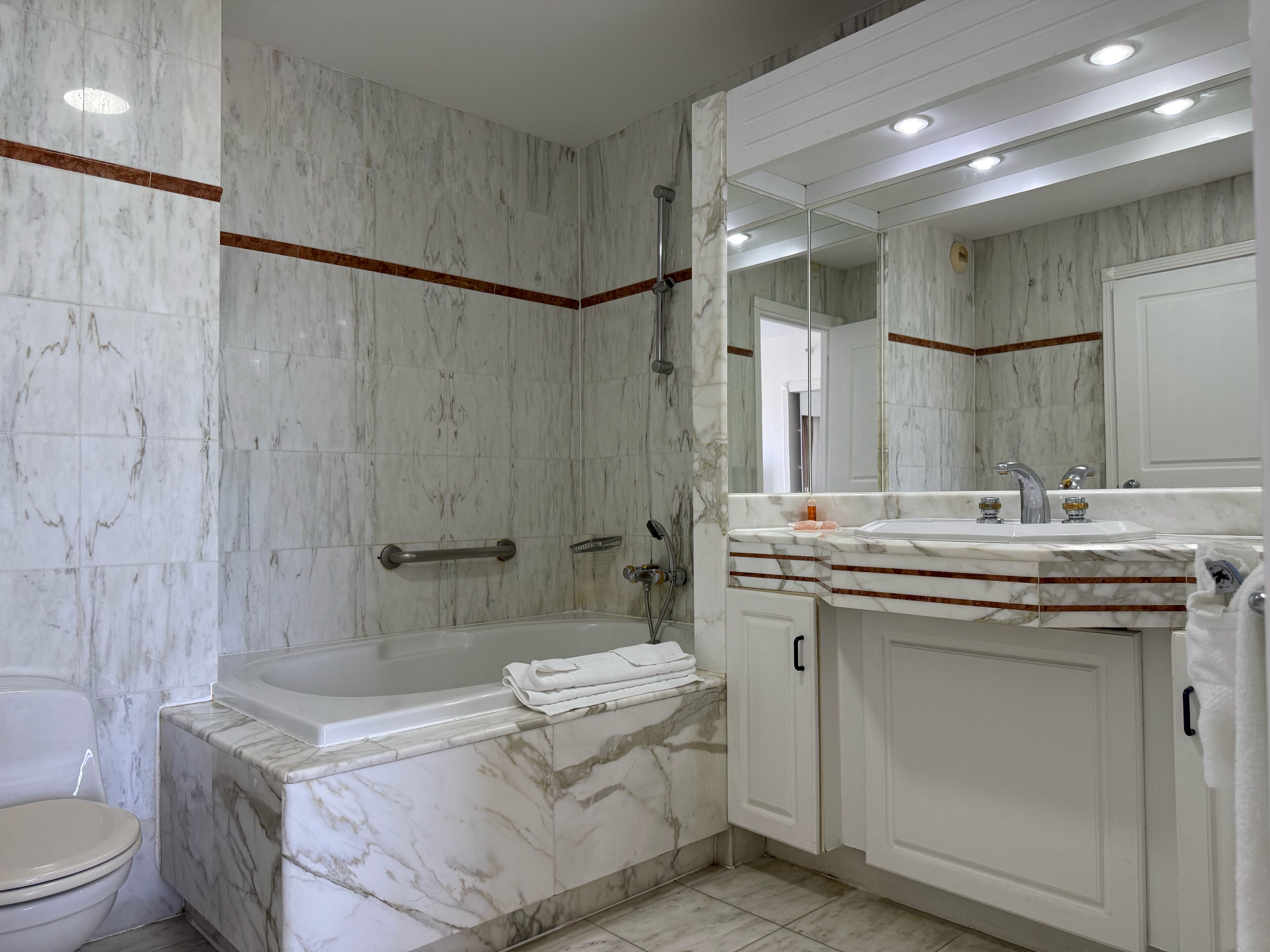 A modern bathroom with a marble sink, a bathtub, and a large mirror.