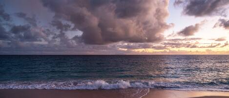 A beach with waves, a clear sky, and clouds.