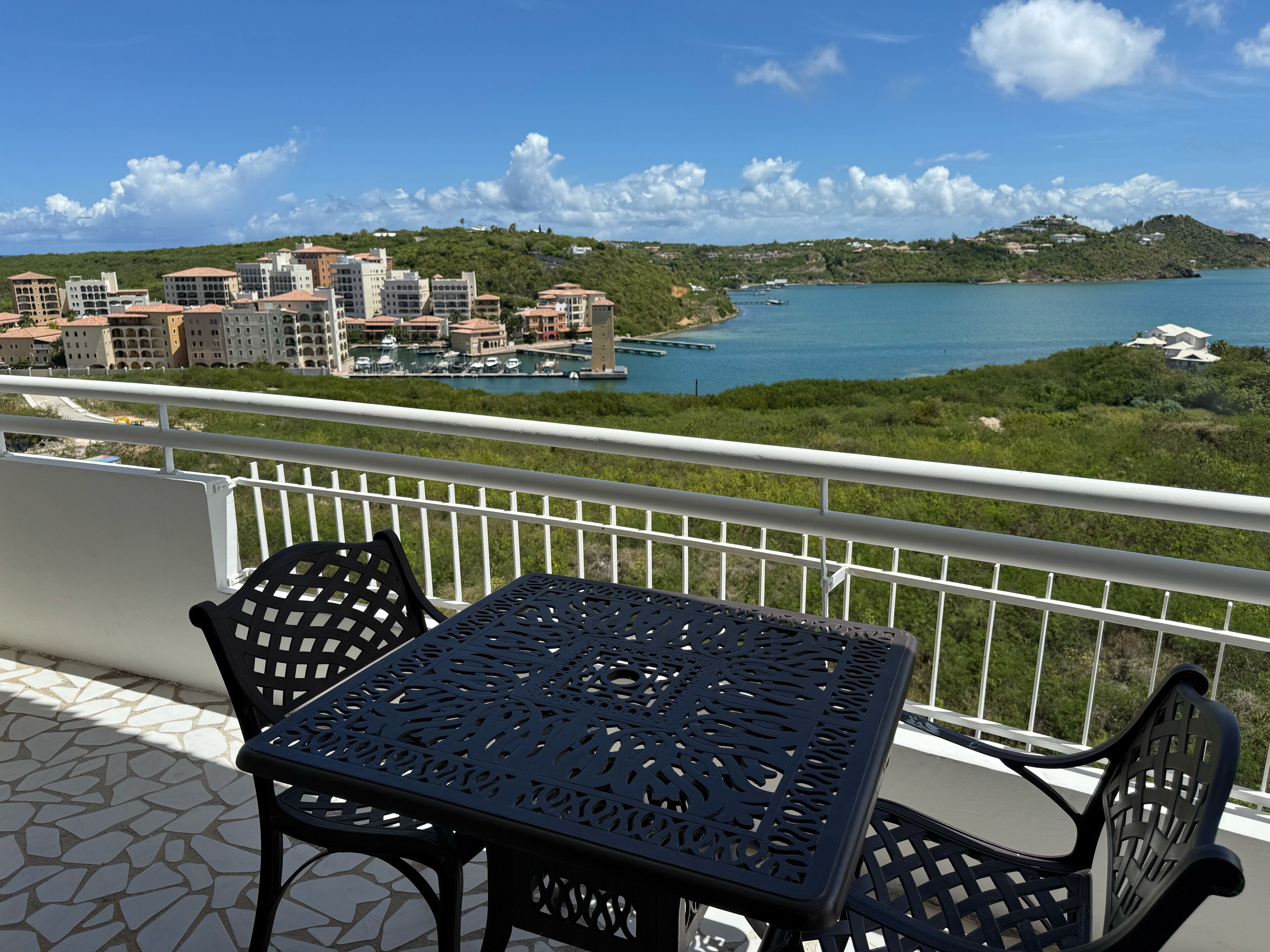 Een balkon met een tafel en stoelen met uitzicht op een jachthaven en gebouwen.