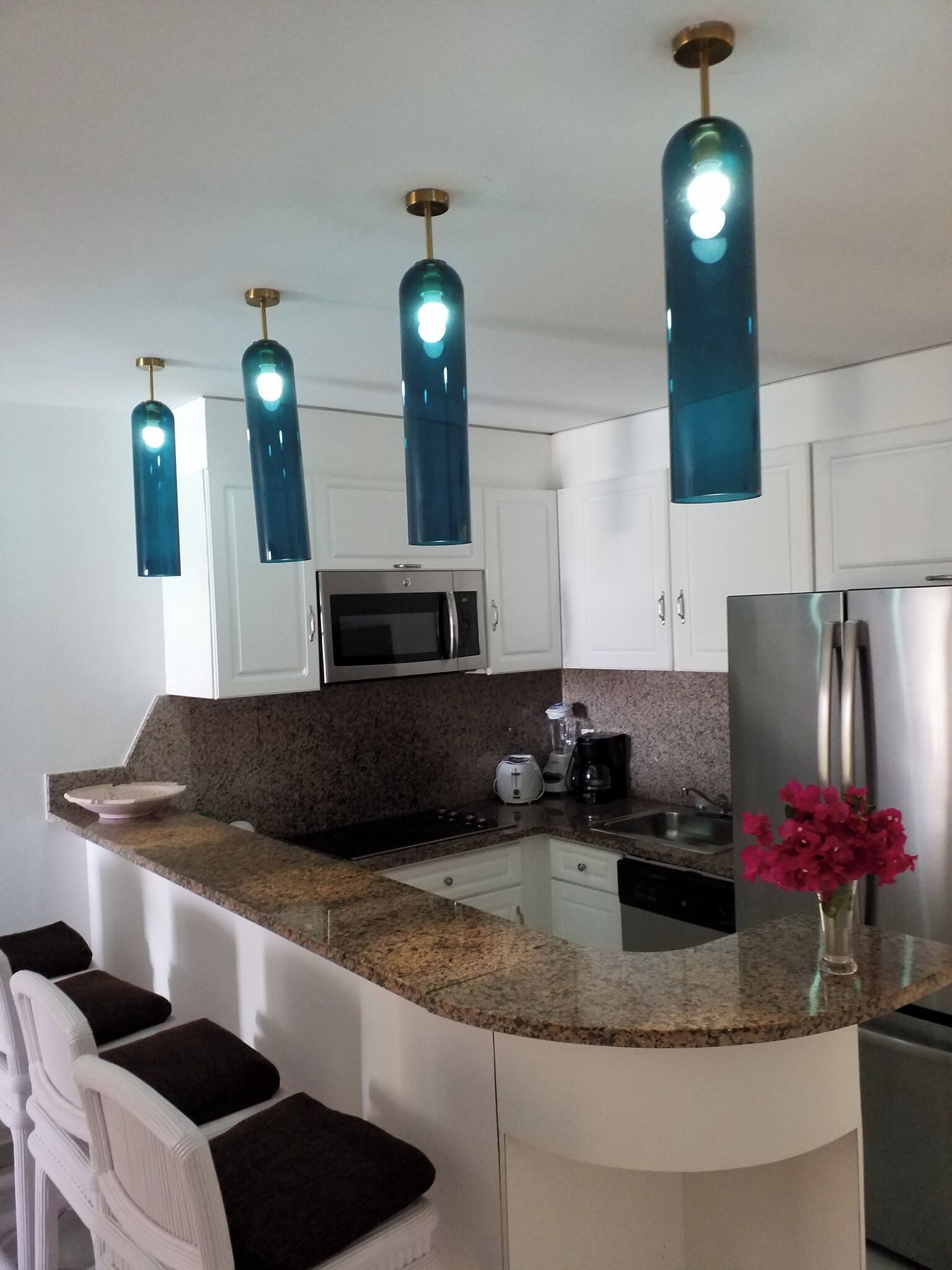 Una cocina moderna con armarios blancos, encimera de granito, microondas integrado, refrigerador de acero inoxidable y una isla central con asientos tipo barra.