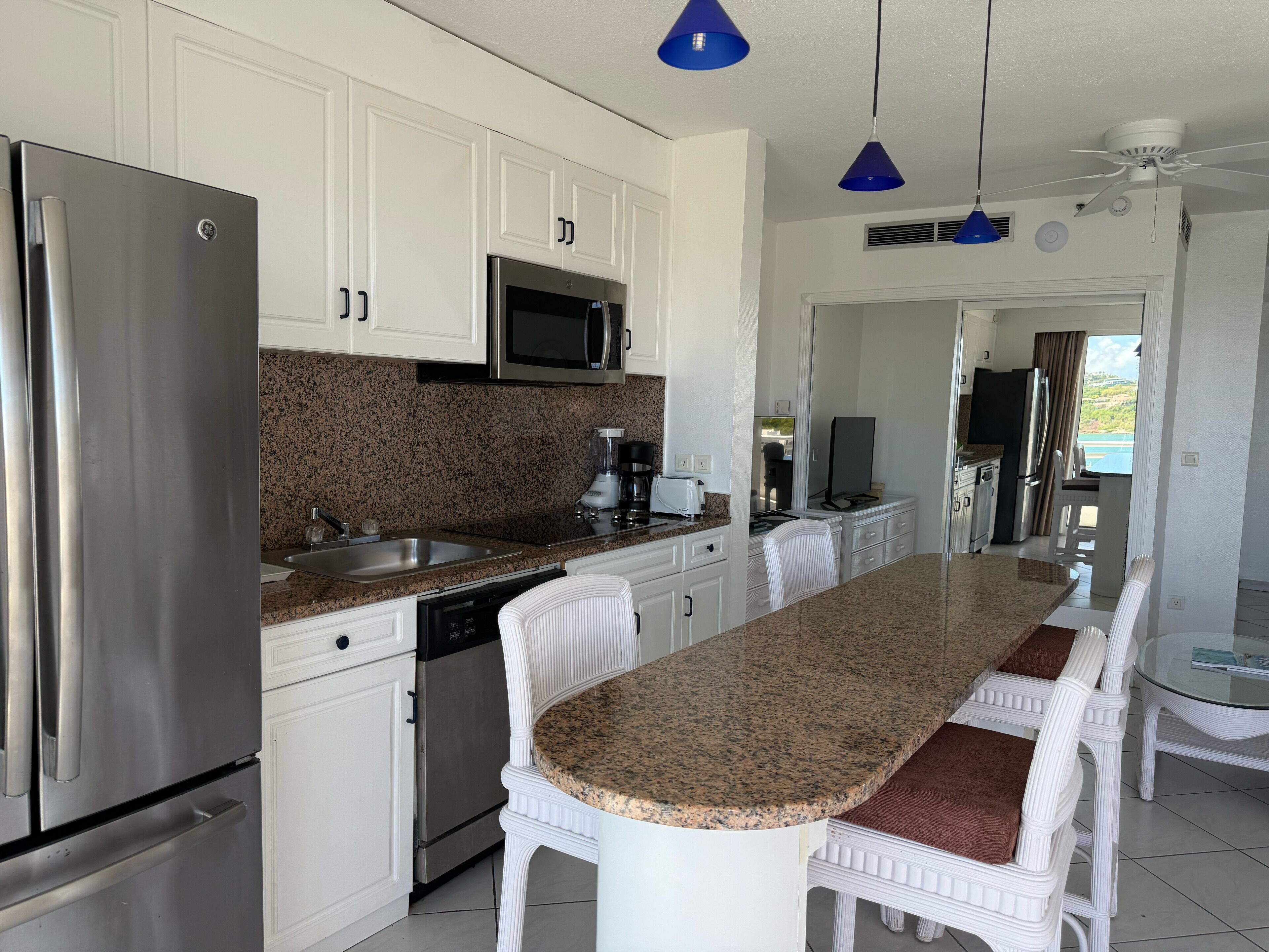 Una cocina moderna con muebles blancos, encimeras de granito y electrodomésticos de acero inoxidable, además de una isla central con asientos.