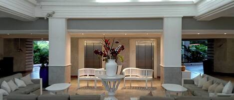 A lobby with a reception desk, two white chairs, a white sofa, and a vase of flowers.