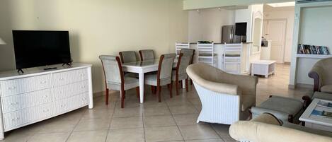 A living room with a TV, dining table, chairs, a white wicker sofa, and a ceiling fan.