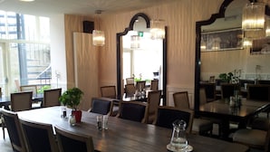 A dining area with wooden tables and chairs, a large mirror, and hanging chandeliers. - The Concert Hotel (Amsterdam)