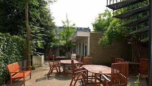 An outdoor patio area with wooden furniture and a brick wall. - The Concert Hotel (Amsterdam)