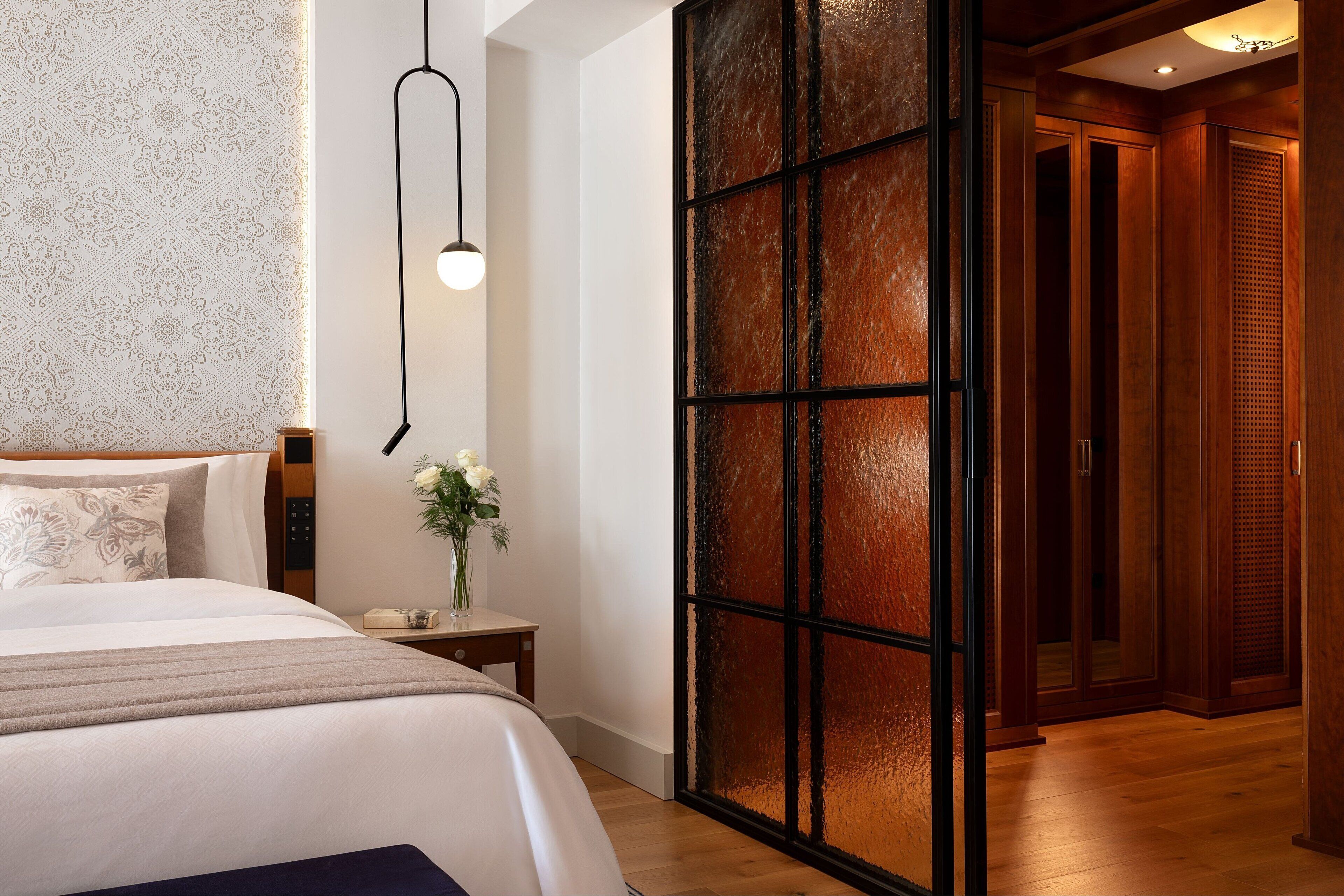 Una habitación de hotel moderna con una cama grande, una mesita de noche con un jarrón de flores, un panel decorativo en la pared y suelo de madera.