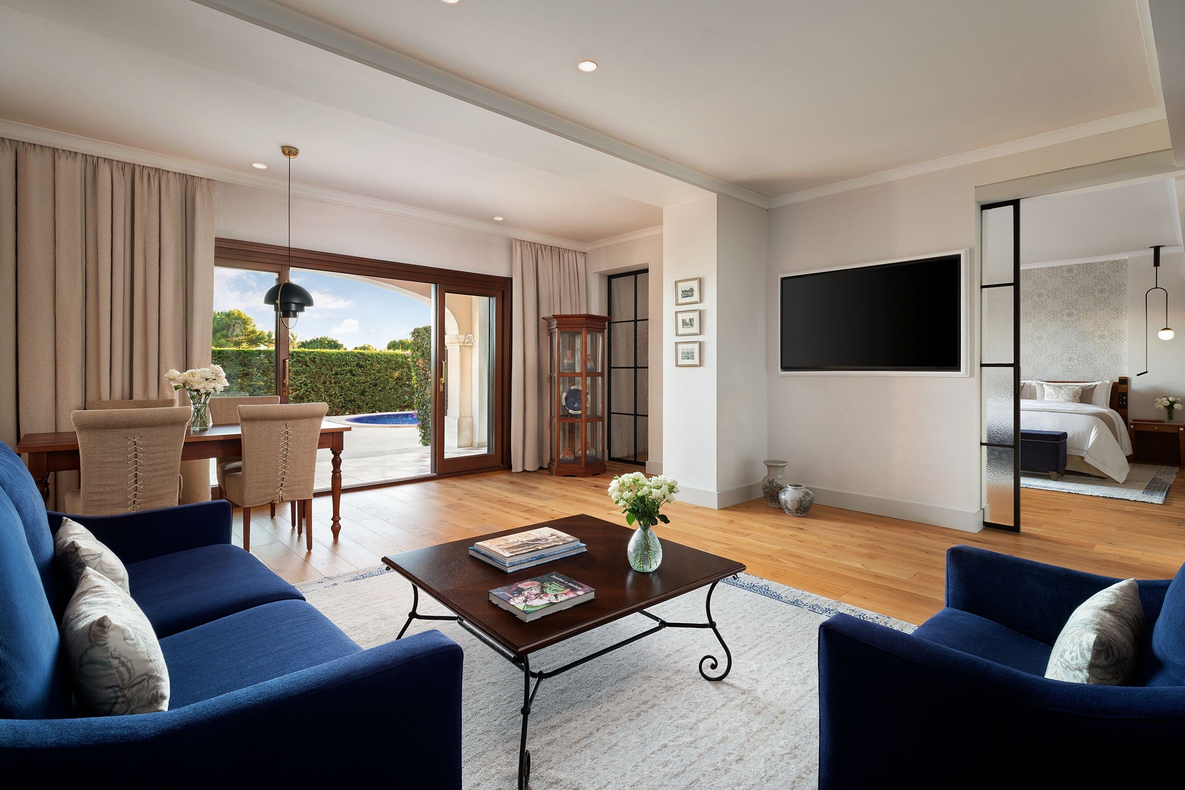 A spacious living room with a large window, a dining area, and a bedroom with a TV.