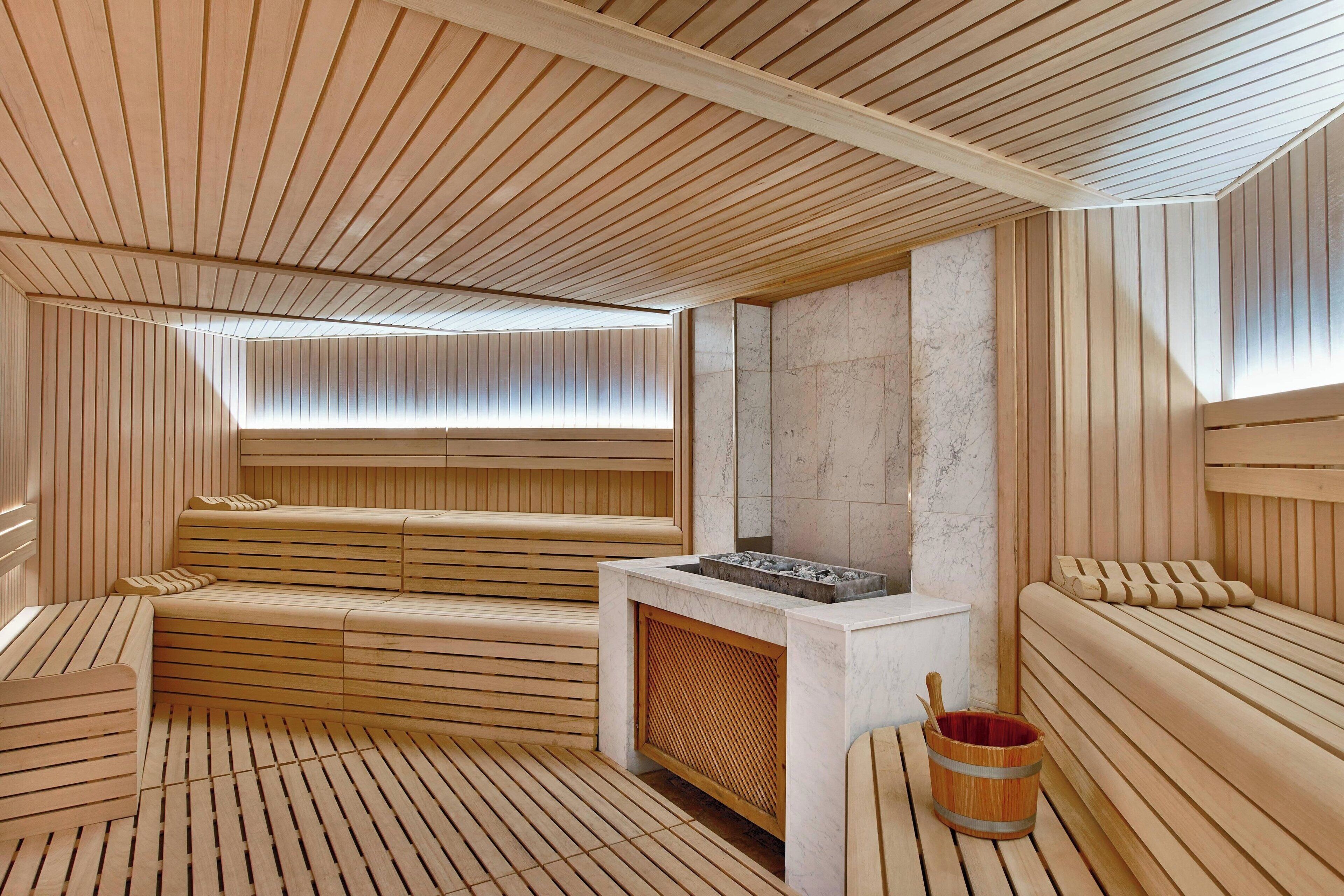 A sauna room with wooden benches, a marble wall, and a wooden bucket.