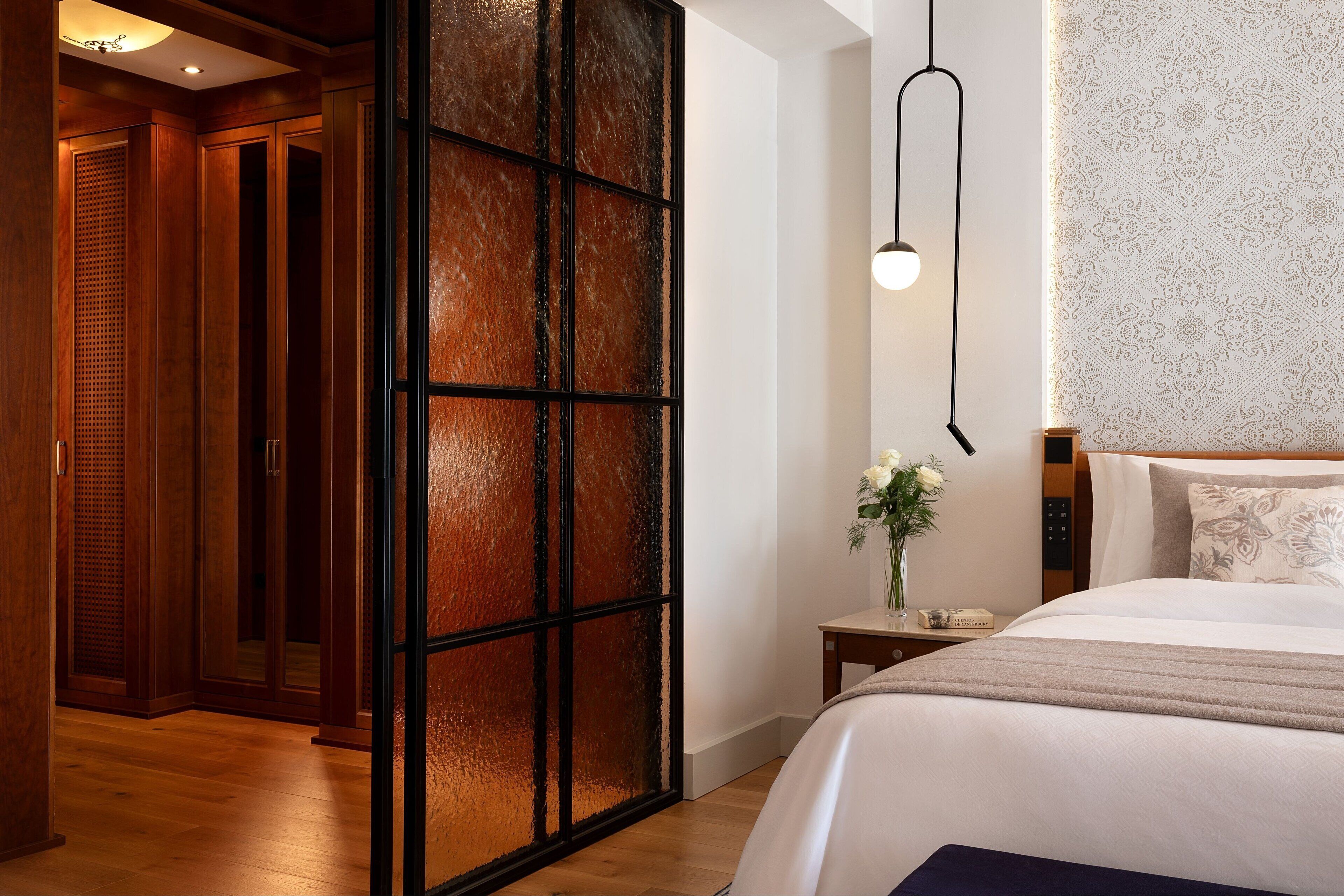 Une chambre d’hôtel avec un grand lit, une table de chevet, un vase de fleurs et une porte coulissante dotée d’un panneau texturé.