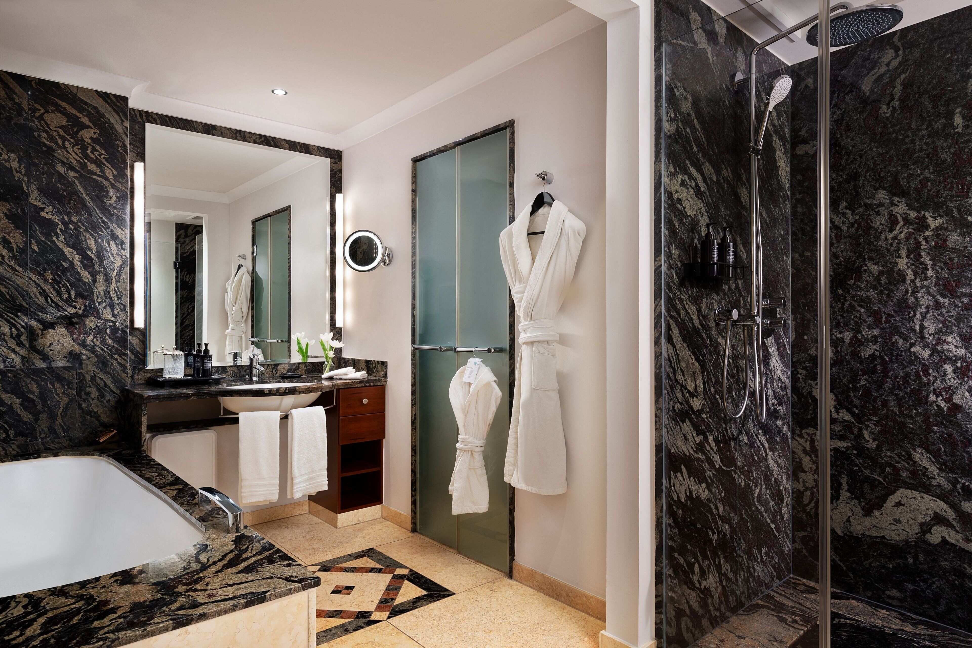 Une salle de bain moderne avec un lavabo en marbre, un grand miroir, une douche en verre et un porte-serviettes.