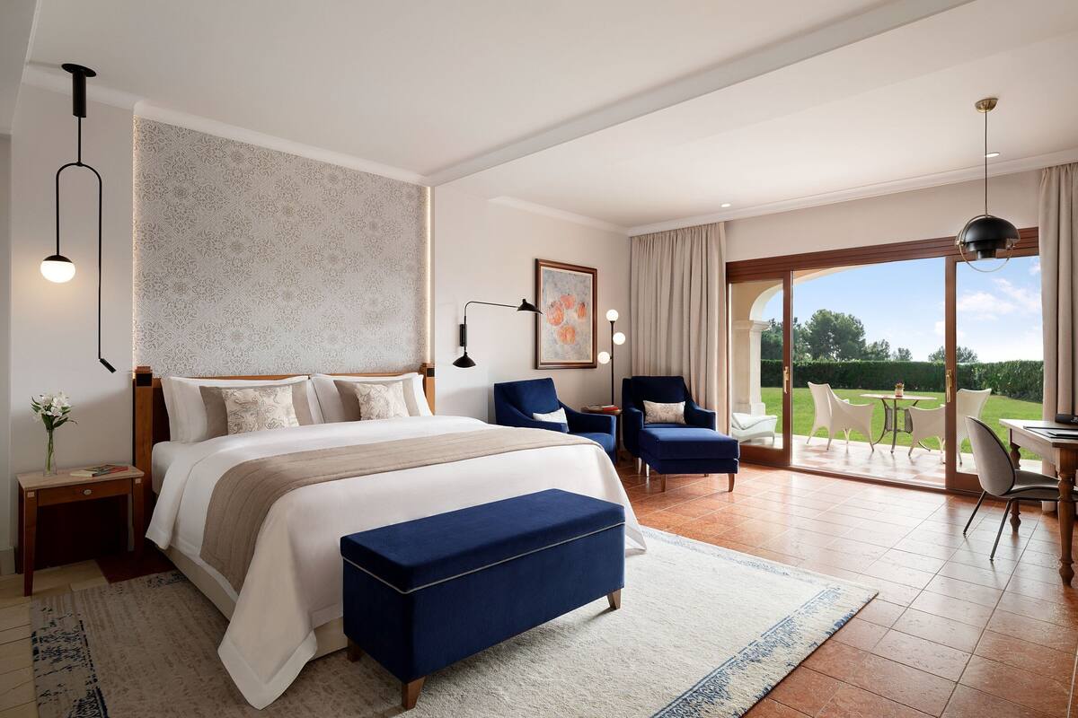 A spacious bedroom with a large bed, a sitting area with chairs, and a balcony with a table and chairs.