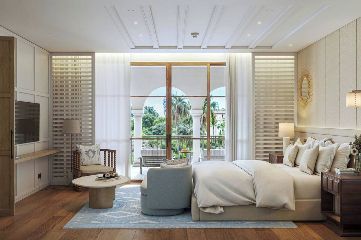 A modern bedroom with a large bed, a TV, a seating area, and a view of palm trees.