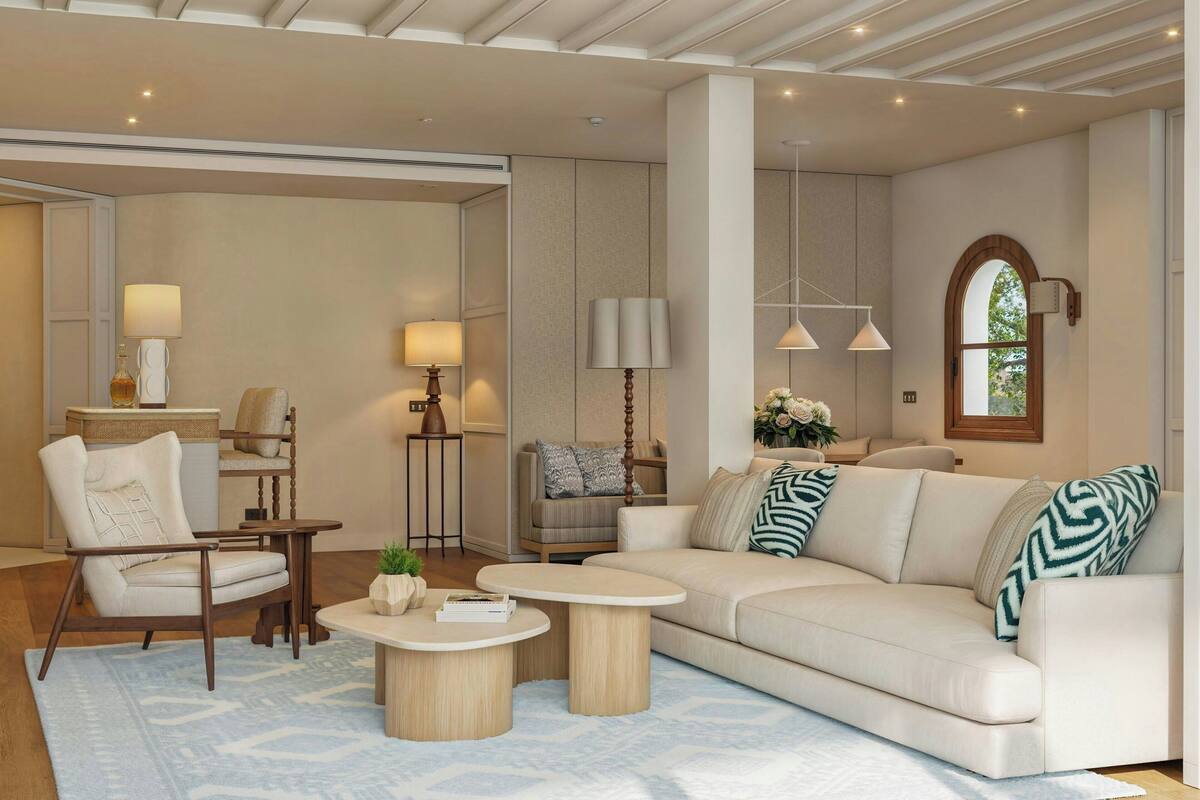 A modern living room with a beige sofa, two round coffee tables, a wooden chair, and a side table with a lamp.