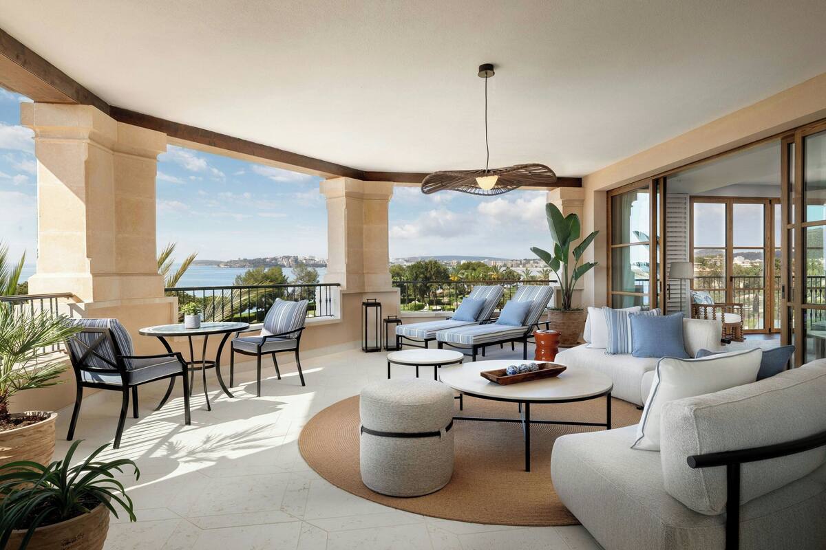 A spacious outdoor seating area with a view of the sea, featuring a round table, sofas, and chairs.