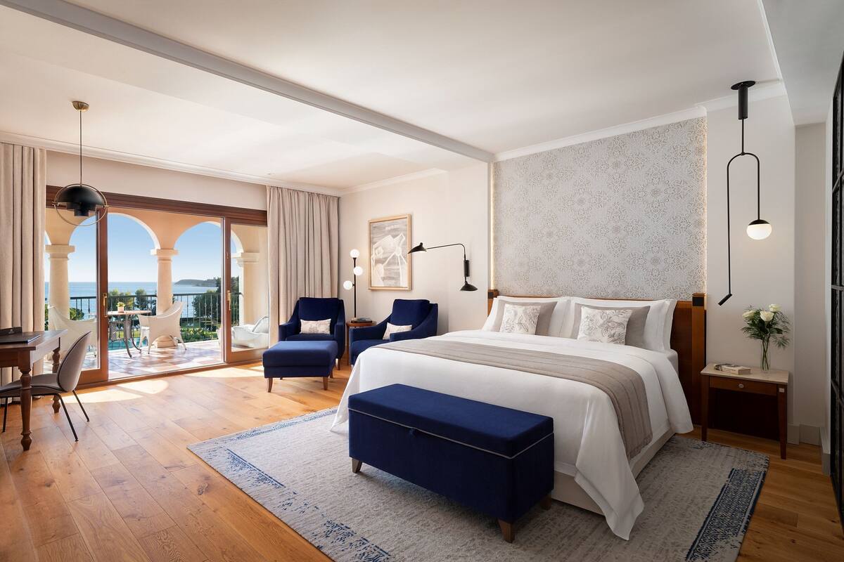 A modern hotel room with a large bed, a desk, and a balcony with a view.